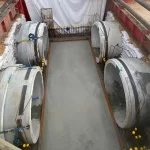 Four large concrete pipe sections are positioned horizontally within a rectangular excavation site lined with sandbags and metal supports.