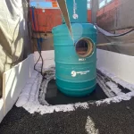 A large blue cylindrical tank labeled "inlet" is installed in a construction pit, surrounded by sandbags and gravel, with workers and barriers nearby.