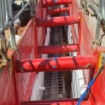 A construction trench with red support beams and metal rebar reinforcement inside, surrounded by safety barriers.